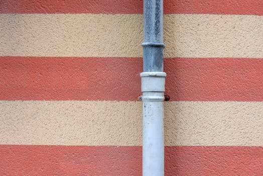 A metal drainpipe set against a red and beige striped textured wall.